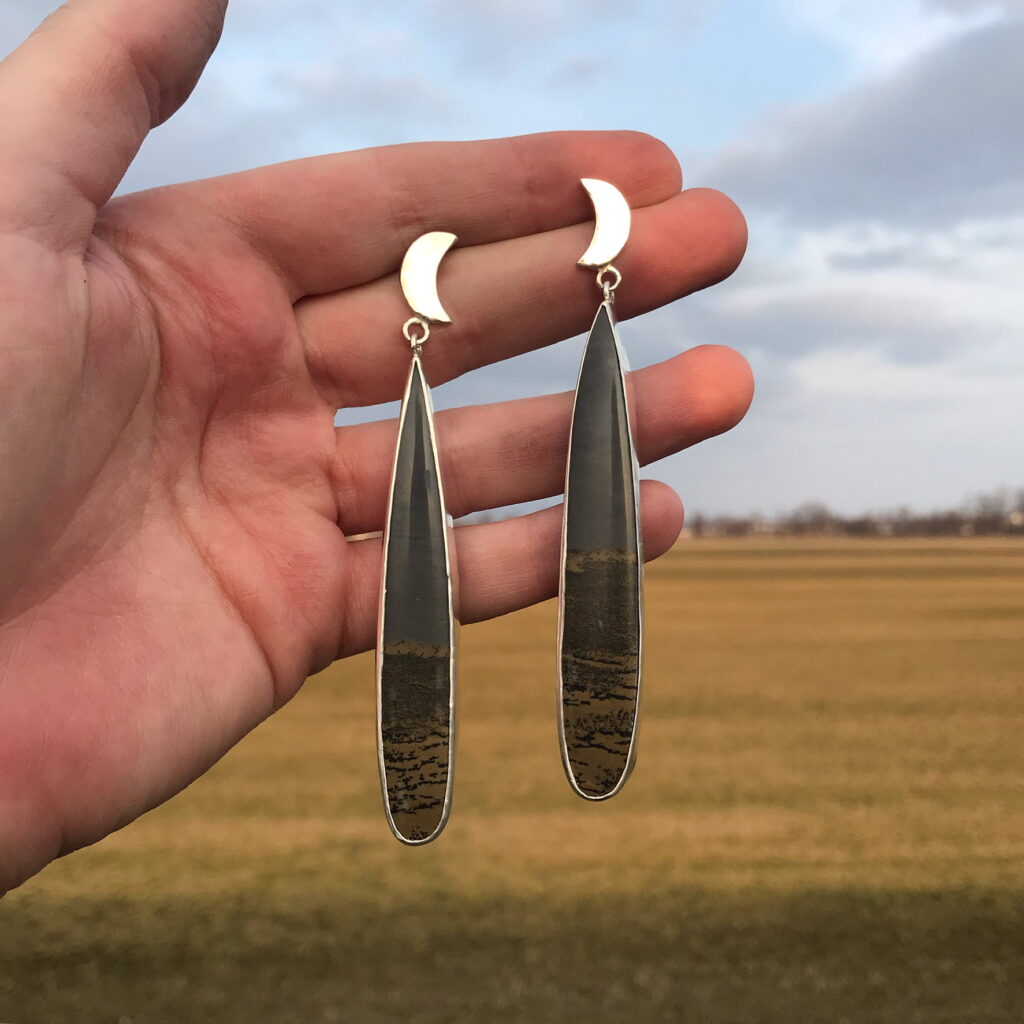 June Metal holds up two handcrafted earrings.